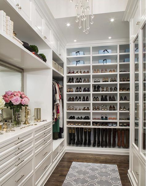 This elegant white closet has customized storage for boots, flats and heels on one long wall. A dresser with a large gilded mirror sits on the far wall, across from glass-faced cabinets. A long, modern chandelier hangs from the soaring ceiling. Organiser Son Dressing, House Closet, Closet Redo, Interior Design Blogs, Organizar Closet, Grand Dressing, Amazing Closets, Walking Closet, Closet Hacks Organizing