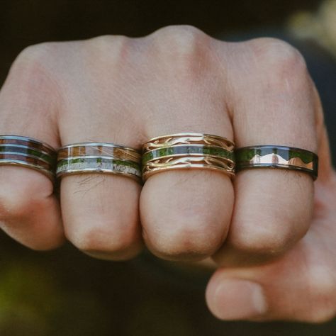 Eight different moss wedding bands from Staghead Designs are shown on a man's left and right hands. These designs include "Vega" flat top band in white gold with moss & ironwood, "Ezra" with moss mountains & whiskey barrel oak, "Rio" with moss, camo, & elk antler, "Remmy" with redwood & moss, "Rio" with moss & redwood, "Dyad" with whiskey barrel, moss, & antler, "Artemis" antler-style band with moss, & "Helios" with moss & rose gold mountains. Moss Agate Mens Wedding Band, Unique Male Wedding Bands, Moss Agate Wedding Rings, Agate Wedding Rings, Earthy Wedding Rings, Moss Agate Engagement Rings, Agate Engagement Rings, Earthy Rings, Boho Wedding Bands