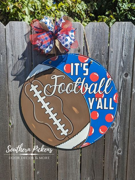 "Celebrate your favorite football team with this customizable door hanger! The lettering and football design are etched into the wood, making for a truly unique piece. Each is hand painted and custom made for each order. Let me know your special requests!  This listing is for a 20\" Circle. Other sizes available upon request. Bow accessory may vary due to ribbon availability, but will always compliment the door hanger in color scheme and design. Shipping notification: Due to being a mom with two House Divided Football, Hanger House, Football Door Hangers, Door Hangers Diy, Door Signs Diy, Football Decorations, House Divided, Being A Mom, Wooden Door Hangers