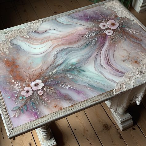 This vintage wooden table boasts a top wrapped in a luxurious layer of pastel-hued resin art, featuring swirls of lavender, dusty rose, and mint green with gold leaf flecks. The edges display intricate lace imprints while its gloss finish mirrors glass.  

#VintageResinArt #ElegantFurniture #PastelInterior #HomeDecorInspiration #VintageWoodTables #ArtisticFurniture Resin Art Table, Pastel Resin, Pastel Interior, Artistic Furniture, Lace Edges, Resin Wall Art, Flower Bird, Elegant Furniture, Painting Flowers