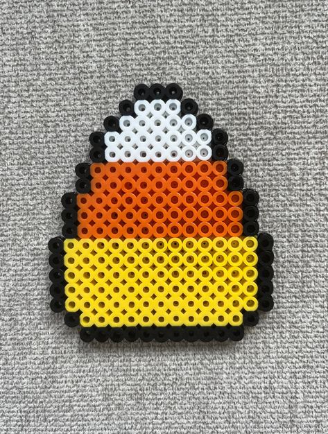 Candy corn perler bead magnet made with yellow, orange, white, and black beads. Cute Food Perler Beads, Perler Bead Patterns With Clear Beads, Peeler Beads Patterns Halloween, Perler Bead Patterns Coraline, Melty Beads Ideas Easy Cute, Perler Bead Magnet Patterns, Melting Beads Ideas Halloween, Camping Perler Beads, Perler Beads Black And White