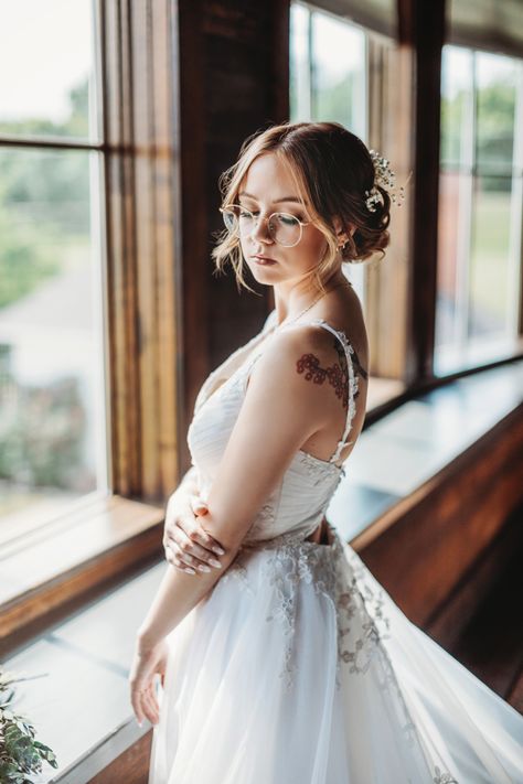 A woman in a wedding dress wearing glasses standing in front of a window Wedding Eye Glasses For Bride, Wedding Eyeglasses Brides, Brides With Glasses Makeup, Wedding Look With Glasses, Wedding Makeup Looks With Glasses, Wedding Hair With Glasses Brides, Bride Glasses Wearing, Wedding Makeup For Glasses Brides, Wedding Dress With Glasses