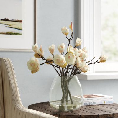 Blossoms that never fade. This faux floral arrangement brings all the freshness and beauty of real flowers to your space without any of the upkeep. Designed to mimic the look of real magnolia blossoms with delicate clusters of white and pink-tinged petals connected to brown, organic-looking branches, they rest in a clear, bell-shaped glass vase that will complement any style of décor. Best of all, the branches are bendable, letting you shape them to suit your style. Flower Color: Pink/Cream | Fr Kitchen Island Floral Arrangement, Magnolia Floral Arrangements, Centerpiece Flower, Dining Room Centerpiece, Flower Colour, Coffee Table Centerpieces, Design Showroom, Faux Floral Arrangement, Magnolia Blossom