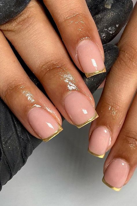 These nails present an elegant take on the classic French manicure with a glossy nude base and striking gold tips. The combination delivers a chic and sophisticated look, perfect for any glamorous occasion.  // Photo Credit: Instagram @gelsbyelisha Nails For 30 Year Olds, French Nails Gold Tip, Short Gold French Tip Nails, Oval Nails Gold, Nude And Gold Nails Short, Clear And Gold Nails, Golden French Tip Nails, Gold French Tip Nails Square, Gold Chrome Nails French