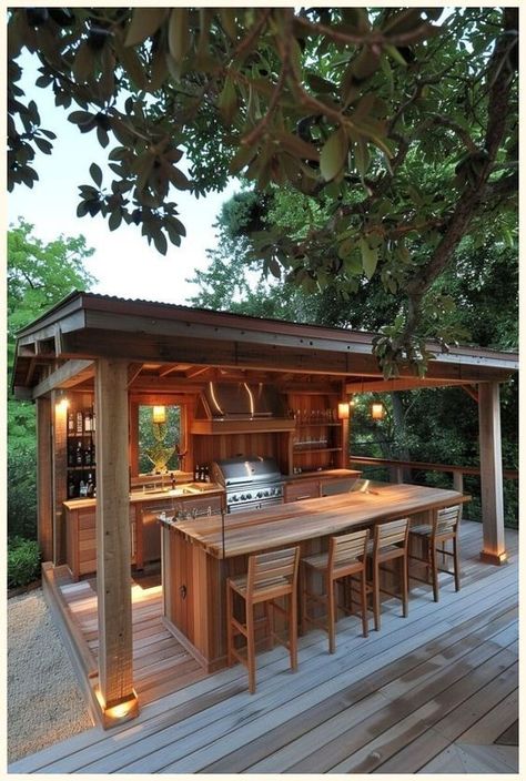 Rustic Outdoor Kitchen1 Outdoor wooden kitchen with bar seating, stainless steel appliances, and warm lighting under a canopy amidst lush greenery. | Sky Rye Design Outdoor Kitchen Modern Farmhouse, Diy Outdoor Kitchen On A Budget, Small Backyard Kitchen, Outdoor Living Space Covered, Covered Grill Area, Garden Kitchen Ideas, Garden Kitchen Outdoor, Summer Kitchen Outdoor, Cheap Outdoor Kitchen Ideas