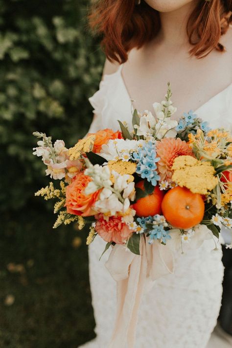 Tangerine inspired bridal bouquet with orange, peach and blue hues Citrus fruits paired with bold florals create the perfect tangerine wedding inspiration. #orangewedding #tangerinewedding #summerweddinginspo #albertaweddings #bridalbouquet #brightcolourscheme #weddingcolours #boldweddingstyle Peach And Orange Bouquet, Winter Citrus Wedding, Citrus Wedding Bouquet, Blue Orange Bouquet, Blue And Orange Table Setting, Tangerine Bouquet, Citrus And Blue Wedding, Blue And Orange Bouquet, Wedding Cake With Orange Flowers