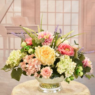 Our designers choose a soothing combination of flowers and hues in soft pinks and greens for this design. Set this beautiful silk floral centerpiece just about anywhere to add color and elegance to your home or office. Created with peonies, ranunculus, soft green and pink hydrangeas, mini roses, berries and foliage. Set in a silver metal low pedestal bowl. Perfect for a dining table, coffee table, dresser, an event or party. | Primrue Faux Silk Arrangement in Vase in Pink | 15" H X 20" W X 14" D Asymmetrical Floral Arrangements, Floral Centerpieces For Dining Table, Summer Floral Centerpieces, Spring Flower Arrangements Centerpieces, Ranunculus Centerpiece, Silk Floral Centerpiece, Seasonal Plants, Pink Flower Arrangements, Table Floral Arrangements