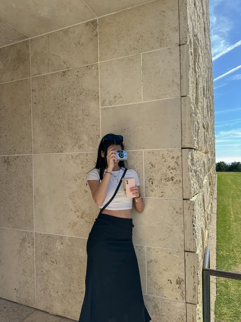 a girl leaning on a building taking a  photo. her camera is covering her face and she is wearing a white crop top and a long black skirt Black Museum Outfit, Cross Body Bag Outfit Summer, Black Cross Body Bag Outfit, Crossbody Bag Outfit Summer, Museum Outfit Spring, Summer Museum Outfit, Ootd Museum, Black Long Skirt Outfit, Museum Ootd