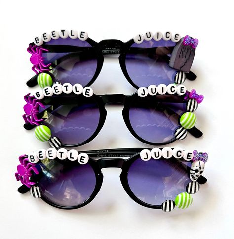 "BEETLEJUICE BEETLEJUICE BEETLEJUICE SUNNIES!! These are so adorable-- Each pair is handcrafted by me. Using various beads, Charms, Rhinestones, and fun details!  🪲  *3 options available-- (see pictured) Choose your style:  1. Graveyard  2. Skull 3. glitter bow  * Anti-Glare * UV Protection (UVA & UVB) * Durable and shatterproof  * They open and close smoothly  * Each item is made to order and will be ready to ship in 5-7 business days! If you need your order sooner. Please check out my \"RUSH ORDER OPTION\".  https://www.etsy.com/EyeCandyandFluff/listing/1286351273/rush-my-order-please *SHOP DISCLAIMER/WAIVER!  * Do NOT let your child put the sunglasses in their mouth as beads can become detached.    Always monitor and supervise while children are wearing these. The shop assumes no respo Beetlejuice Jewelry Diy, Halloween Sunglasses, Halloween Glasses, Beaded Sunglasses, Teacher Appreciation Gifts Diy, Festival Sunglasses, Personalized Sunglasses, Beetlejuice Beetlejuice, Oh My Goddess