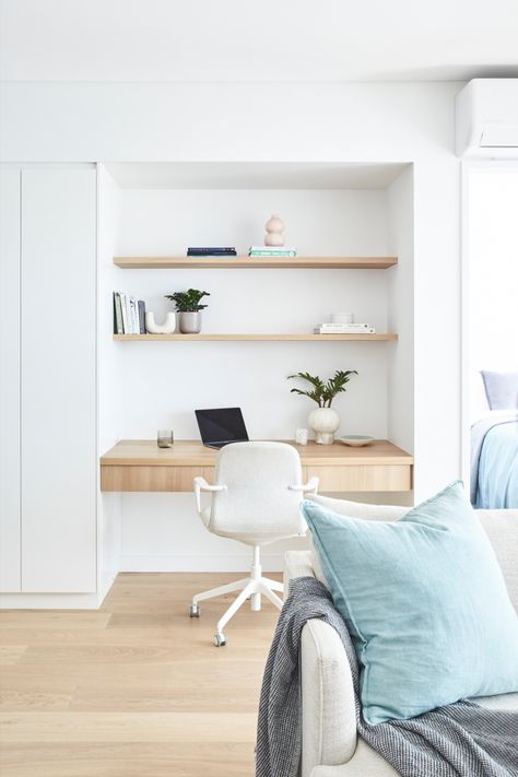 Inner-city apartment renovation showing a study nook built next to custom white joinery. The study nook features a pale timber floating desk with drawers & open timber shelving above. The shelves are styled with books, plants & ceramic items. A white office chair also sits at the desk behind an open laptop. The edge of an off-white sofa with a pale chambray blue cushion and blue-grey throw can be seen in the foreground. The master bedroom, in similar tones of blue, can be seen just out of frame. Built In Office Nook In Living Room, Hamptons Study Nook, Desk Alcove Built Ins, Linen Cupboard Study Nook, Study Nook Cabinetry, Study Nook In Kitchen, Built In Workspace, Built In Study Nook, Study Nook In Bedroom