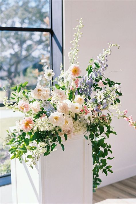 Stylish florals for weddings + events, and a Daily Delivery Flower Shop that allows us to give back to our community through "Floral Support." Based in Austin, Texas. The Arlo | Stems Floral Design | Sarah Stipanovich Photography Bright, modern indoor ceremony space with pastel floral arrangements on pedestals. Hints of pink, purple, blue and peach flowers. Blue White Pink Flower Arrangements, Peach And Blue Wedding Flowers Centerpieces, Pastel Floral Wedding Arch, Spring Pastel Floral Arrangements, Mixed Pastel Wedding Flowers, Blue Peach Flowers, Faux Floral Arrangement Wedding, Peach Pink Blue Wedding, Spring Wedding Arrangements