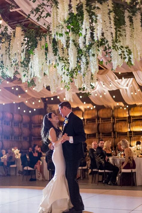 A large ceiling installation above the dance floor is a stunning focal point to a gorgeous white winter wedding. Filled with white flower and greenery hanging in an organic way the newly weds share a dance under the hanging flowers. Wedding Flower Ceiling Decor, Florals Hanging From Ceiling Wedding, Hanging Flower Installation Wedding, Hanging Floral Arrangements Wedding, Wedding Ceiling Decorations Flowers, Hanging Flowers Wedding Reception, Flowers Hanging From Ceiling Wedding, Flower Ceiling Wedding, Classical Color Palette