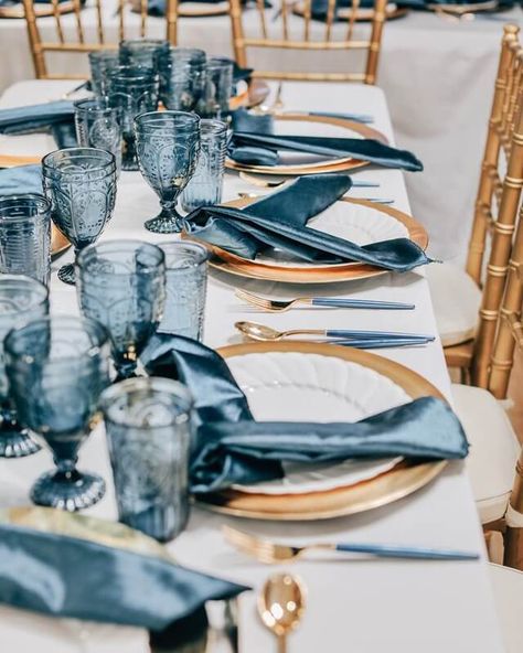 Create a stunning tablescape at your special event by dressing up your tabletop with a whimsical white tablecloth. Impress your invitees by pairing up white dinner plates and gold chargers with gold cutlery and dusty blue napkins for a presentable display. Lastly, add finishing touches to your gorgeous table setup by bedecking your gold party chairs with comfy white chair pads. Blue And Gold Tablescape, Blue White And Gold Party Decor, Bachelorette Table Decor, Dusty Blue Napkins, Blue Dinner Party, Bachelorette Table, Chargers Plates, Elegant Table Decor, Blue Cloth Napkins