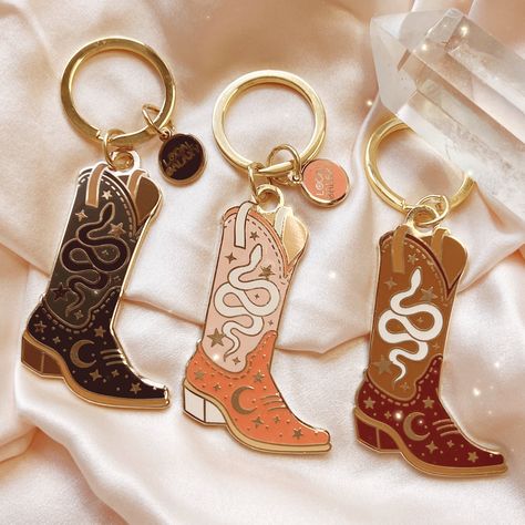 "Our cowgirl boot keychain is designed with the cosmic cowgirl in mind, featuring icons related to the moon goddess including a serpent & crescent moon.  Available in 3 colors: Blush Pink, Black & Brown.  Hard enamel keychain with gold tone detailing.   We are proud to be a member of 1% for the Planet 🌎 ▽. * Measures approx. 2 1/4\" high x 1 1/2\" wide * Features our original, Local Galaxy illustration * Hard enamel with soft, gold tone plating  * Packed on our signature backing card & cotton g Cowgirl Keychain, Cowboy Boot Keychain, Boot Keychain, Galaxy Illustration, Cowgirl Things, Cosmic Cowgirl, Cowgirl Stuff, Enamel Keychain, Cowgirl Gifts