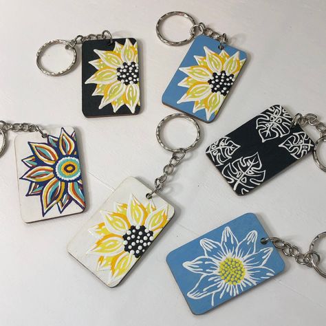 "This hand painted, dual sided sunflower keychain features festive multi colored petals that rest on a white background. Side A features a single, partial sunflower, and side B features partial sunflowers in opposing corners. Keychain is 2\" x 1.3\" and is sealed to prevent scratches or dampness it could incur while accompanying your keys." Hand Painted Fridge Magnets, Hand Painted Keychain, Keychain Painting Ideas, Wood Keychain Ideas, Keychain Painting, Keychain Diy Easy, Stylized Foliage, Painted Keychain, Painted Magnets