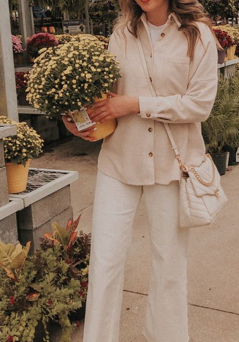 The photo is zoomed in on Carolynn's outfit. She's holding a pot of yellow flowers on her right hip and walking. She's wearing a beige corduroy shacket, white Boxy T-Shirt, white Wide Leg Jeans, and a white quilted handbag with gold chain Cream Button Up Outfit, White Corduroy Shirt Outfit, Beige Corduroy Shirt Outfit, Beige Shirt Outfit Casual, Cream Shirt Outfit Women, Beige Wide Leg Jeans Outfit, Beige T Shirt Outfit, Cream Wide Leg Jeans Outfit, Cream Shirt Outfit