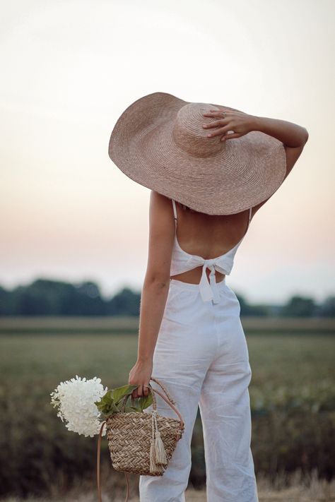 Annie B. standing in field watching sunset in oversized straw hat and white linen jumpsuit taken from behind Outfit With Straw Hat, Woman From Behind, Swimsuit Shoot, White Linen Jumpsuit, Watching Sunset, Open Dress, Oversized Hat, Linen Jumpsuit, Straw Hats