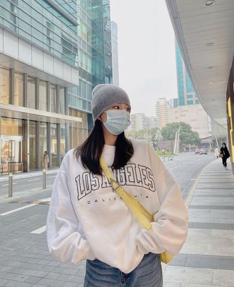 girl standing maybe in seoul korea wearing a beanie and face mask. has her hands in her jean pockets and is wearing a white los angeles over sized sweather with yellow crossbody bag Outfit Inspo Asian, Street Style Seoul, Chinese Street Style, Korean Style Outfit, Fashion Beanie, Girl Streetwear, Seoul Fashion, Fashion Korean, Seoul