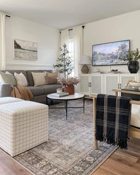 Round white and black coffee table for grey couch stands on a grey vintage rug in this modern farmhouse living room. The table is placed in front of a white cane TV cabinet holding a taupe and white table lamp. Rug Dark Couch, Grey Couch Natural Living Room, Gray Couch Living Room Rug Ideas, Modern Organic Living Room Brown Couch, Light Grey Couch Accent Pillows, Light Gray Couch Green Accents, Gray And White Living Room Ideas Cozy, Dark Grey Couch With Rug, Country Living Room Grey Sofa