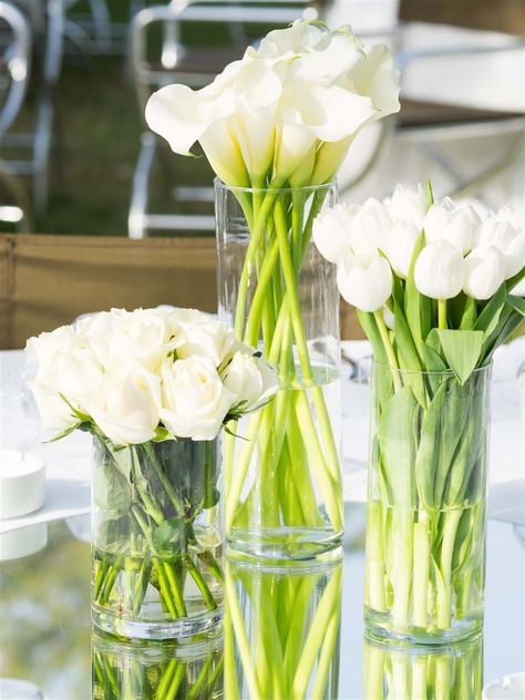 A trilogy of white roses, callas and tulips create a modern and minimalist wedding table decor | Athens Wedding Planner & Designer: @mitheoevents Photo: @JohnNassari Venue: @islandathens | #mitheoevents #weddingplannergreece #destinationweddingplanner #athenswedding #luxurywedding #iranianwedding #athensrivierawedding #weddingstyling #weddingdecor #allwhitewedding #tablesetting #tablescape #tabledecor #weddingflorals #whiteweddingflorals Floral Arrangements For Table, Tulip Centerpieces Wedding, Tulip Wedding Decorations, Tulip Table Decor, Wedding Centerpieces On A Budget, Chic White Wedding, Tulip Centerpiece, Black And White Wedding Theme, White Floral Arrangements