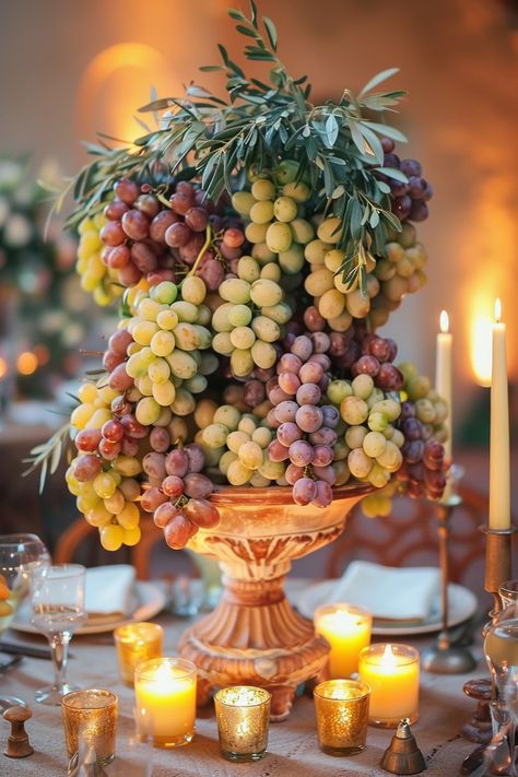 ✨ Elevate your wedding ambiance with a centerpiece that whisks you away to the rolling hills of Tuscany. Experience the charm of Italy as grape vines & olive branches intertwine with the warm glow of candles on your special day. #WeddingInspiration #TuscanWedding #RomanticDecor #WeddingIdeas #CountryChic #RusticElegance #GrapeAndOlive #CandlelightMagic Let the light guide your love story. Grapes Centerpiece Wedding, Tuscany Rehearsal Dinner, Olive Branches Decor, Italian Themed Tablescape, Olive Theme Party, Greek Tablescape, Round Tablescapes Wedding, Grape Wedding Theme, Greek Table Setting