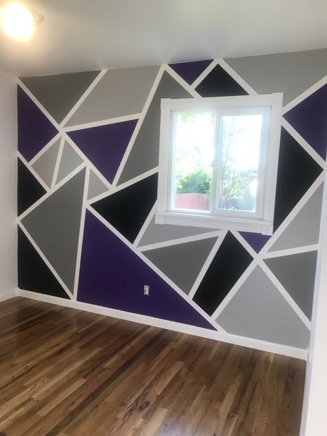 When your son says he would like to use hot rod purple and black for colors in his room...you become resourceful! Made this geometric accent wall with painting tape. Added two shades of grey to the mix. Found this idea on Pinterest!!🖤💜🖤💜🖤 If you paint the tape edges first the same color as your background, your lines will be perfect. Instead of “bleeding” the main color they “bleed” invisible. Do not let dry long, just enough so you can paint your main colors. Tape comes off easy then. Purple And Black Geometric Wall, Purple And Grey Walls, Tape And Paint Walls, Accent Wall Bedroom Purple Grey, Purple Bedroom Paint Ideas, Blue And Purple Wall Paint Ideas, Black Grey Purple Bedroom, Purple Wall Design Paint, Purple And Grey Room Ideas