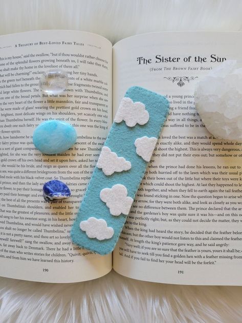 A light blue bookmark with white clouds sitting ontop of a book, surrounded by crystals. Foam Sheet Bookmarks, Gifts With Wool, Felt Bookmarks Handmade, Sewing Bookmarks Diy, Bookmark Clouds, Bookmark Handmade Ideas, Punch Needle Bookmark, Felt Book Marks, Bookmarks Handmade Easy