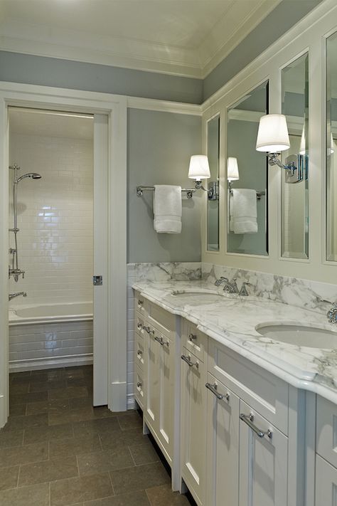 White and gray bathroom with white farmed mirrors on blue gray walls over white double vanity topped with white and gray countertops as well as pocket door leading to separate shower space featuring subway tiled drop-in tub accented with white subway tiled shower surround. Bathroom Lighting Over Tub, White Subway Tile Shower, Blue Grey Walls, Faucets Bathroom, Grey Countertops, Double Vanity Bathroom, Shower Surround, Trendy Bathroom, Blue Bathroom