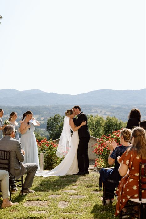 bride and groom stand in front of their friends and family and share their first kiss. In the background are mountains and the tuscan countryside. Wedding Ceremony Kiss Pose, Wedding First Kiss Photo, Wedding First Kiss Pose, First Kiss Pose Wedding, Wedding Ceremony Kiss, Wedding First Kiss, Ceremony Kiss, First Kiss Wedding, Kiss Wedding