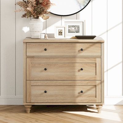 This 3-drawer dresser adds farmhouse-inspired charm and lots of storage space to your bedroom or guest room. It's made with high-grade certified wood in an ivory finish that's distressed for a rustic feel, and it rests on turned feet for a classic silhouette. The three drawers have ring pull hardware in an antiqued bronze finish. Plus, they give you plenty of room to organize your sweaters, shirts, and more. At nearly 34" wide, this dresser's surface makes a great platform for a lamp and vase of Cottage Core Bedroom Dresser, Light Stained Dresser, Mcgee Master Bed, Light Wood Chest Of Drawers, Light Wood Nightstand Bedside Tables, Bedside Chest Of Drawers, Guest Room Decor On A Budget, Non Matching Bedroom Furniture Ideas, Small Dressers For Bedroom