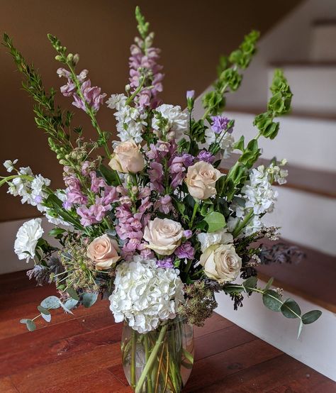 A lovely mix of spring blooms in tranquil shades of white, green, lavender and peach. This garden style bouquet may include: bells of Ireland, stock flower, snapdragons, carnations, hydrangea, roses, waxflower, and mixed greens. Upgrade to transform this design from "front-facing" to "360 degrees".   We use only the fr Purple White Green Flower Arrangements, English Garden Flower Arrangements, Wide Flower Arrangements, Green And Purple Flower Arrangements, Snapdragon Flower Arrangement, Stock Flower Arrangements, Jw Memorial Flowers Arrangements, Easter Bouquets Floral Arrangements, March Flower Arrangements