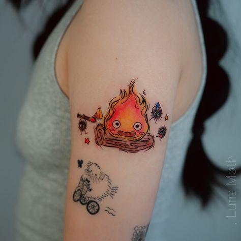 . This beautiful tattoo by our artist Judy @juju_tatt brings the enchanting world of Hayao Miyazaki to life! Featuring Calcifer, the spirited flame from *Howl’s Moving Castle,* and the soot sprites from *Spirited Away,* this piece captures the magic and whimsy that Miyazaki is famous for. Judy has expertly translated these beloved characters into a design that’s both nostalgic and visually stunning. Whether you’re a lifelong fan of Studio Ghibli or simply appreciate the artistry, this tatto... Calcifer Art Tattoo, Howl's Moving Castle Tattoos, Calsifer Howl Tattoo, Calciferol Tattoo, Studio Ghibli Calcifer Tattoo, A Heart Is A Heavy Burden Howl Tattoo, Calcifer Pumpkin, Howls Moving Castle Tattoo Small, Studio Ghibli Sleeve Tattoo