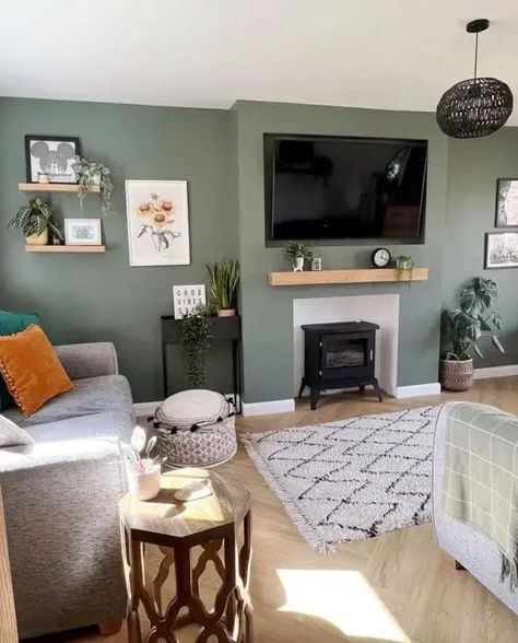 Picture of a cool green living room with a hearth, some shelves, a TV, a grey sofa with pillows, a a rug and some lovely and cool decor Grey Sofa With Pillows, Grey Living Room Decor Ideas, Green And Grey Living Room, Green Living Room Color Scheme, Living Room Design Green, Sage Living Room, Gray Sofa Living, Green Walls Living Room, Sofa With Pillows