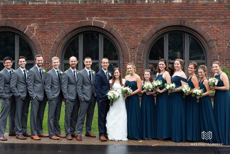 Groomsmen wearing gray suits and bridesmaids in navy dresses. Navy Blue Wedding Bridal Party, Navy Bridesmaids And Grey Groomsmen, Navy And Gray Wedding Party, Navy Blue Bridesmaids And Groomsmen, Navy Groomsmen Suits And Bridesmaids, Navy Bridesmaids And Groomsmen, Dark Grey Groomsmen Suits, Navy Blue And Grey Wedding, Dark Grey Groomsmen