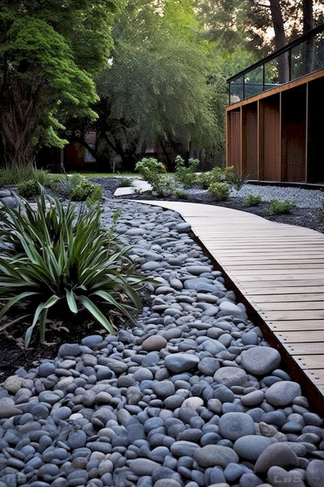 Create a stunning outdoor path with rocks, wood, and dark aquamarine and gray tones. Achieve a sleek and decorative look that is both lush and detailed, yet clean and simple. Grey Rocks Landscaping, Dark River Rock Landscaping, Garden With River Rocks, Grey Rock Landscaping, Gray Rock Landscaping, Garden With River, River Rock Path, Dry Riverbed Landscaping, Diy Rock Garden