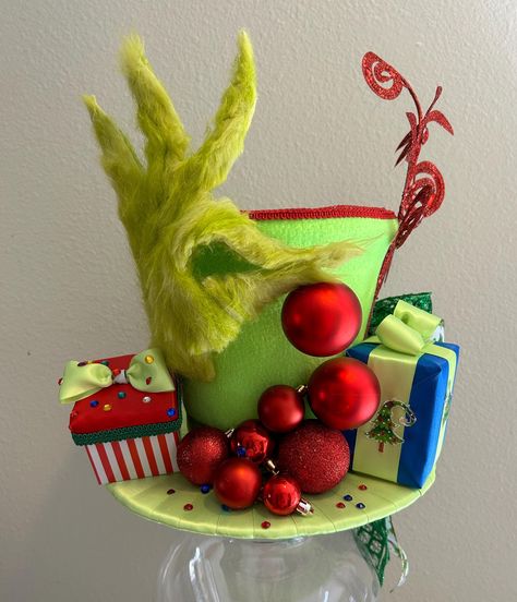 This fun Christmas Grinch tree topper top hat/centerpiece is READY TO SHIP. Use it as a Christmas tree topper or a Christmas decoration centerpiece.   The top hat is uniquely made with a cavity opening on the top and bottom. The bottom is used to insert the tree branch and secure the hat. The top opening allows you to add more sprays, plumes, or decorative items to make a larger and more elaborate tree topper or use it as a decorative centerpiece. Our top hat tree toppers/centerpieces are 100% handmade by us with high-quality materials. The designs are unique design. Our top hat tree toppers/centerpieces stand alone in design, appearance, craftsmanship, quality, and originality. For Decorative Use Only! 0111202023 The Grinch Tree Topper, Grinch Hat Diy, Grinch Hats, Grinch Tree Topper, Top Hat Christmas Tree Topper, Dr Seuss Trees, Top Hat Christmas Tree, Hat Christmas Tree Topper, Christmas Top Hat