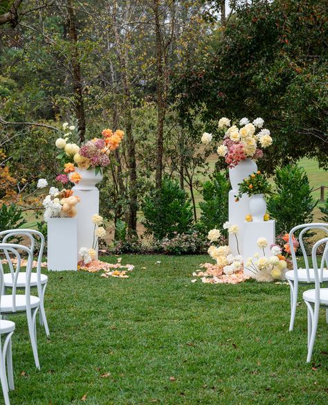 There's been a huge return to the elevated plinth style ceremonyscape, though with a modern twist as seen here with our citrus inspired colour crush. With accenting pedestals and contemporary pot groupings, and ground flower clouds with light scattering of petals to accent your colour palette it's a popular design choice for a sophisticated floral design. Image @marcusbell @studioimpressions Venue @spicersclovellyestate @spicersclovellyweddings Decor @lovebirdweddings ⁠ Pedestal Altar Wedding, Pedestal Wedding Decor, Free Standing Flower Arrangements Wedding Ceremony, Aisle Ground Flowers, Wedding Plinths With Flowers, Floral For Ceremony, Pedestal Flowers Wedding Ceremony, Pedestal Arch Wedding, Ground Flowers Ceremony