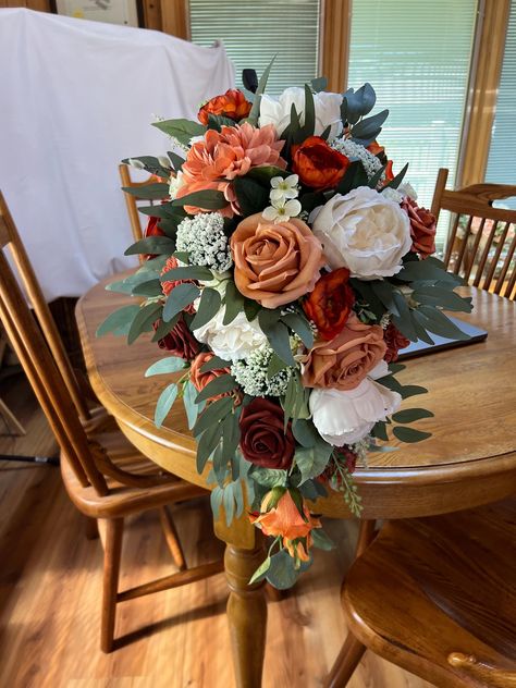 This is a fall cascade of terracotta, cream, burnt orange, and peach with sage colored greenery. Inspired by The color collection Terracotta Sunset this bouquet will be beautiful for your fall wedding.  It is made on a traditional bouquet holder that can be wrapped in ribbon or burlap to conceal.  It is 22 inches long. Also pictured are large round bridesmaids bouquets. I can created pieces for your entire wedding party if you choose. Terracotta Cascading Bouquet, Champagne And Terracotta Wedding Theme, Terracotta Flower Bouquet, Wedding Bouquets With Roses, Spice Wedding Colors, Faux Flower Arrangements Wedding, Maroon And Burnt Orange Wedding, Terracotta Flowers Wedding, Mums Wedding Decor