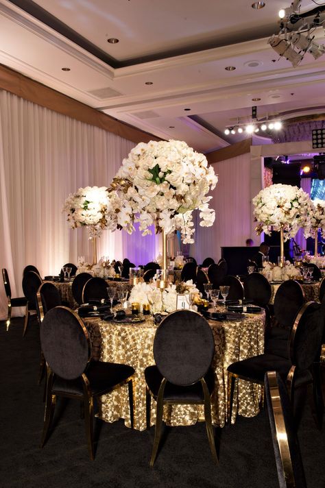 For their golden 50th anniversary party, guests sat at round tables covered with gilt linens and surrounded by black velvet chairs. Centerpieces showcased tall… Centerpiece For Anniversary Party, 50 Anniversary Table Centerpieces, 50th Anniversary Party Ideas Decoration, 50th Wedding Anniversary Party Ideas, 50th Anniversary Table Decorations, Golden Anniversary Decorations, 50th Anniversary Table, Surprise Vow Renewal, Gold Anniversary Party