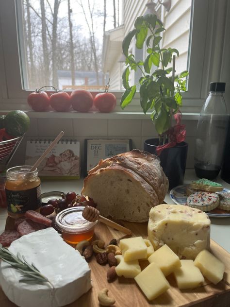 Photo of a grazing board on a white counter with red grapes, a loaf of bread, and cheese in a wheel with a rosemary garnish and cubed cheeses with nuts and honey near. There are herbs on the counter. Cheese Astetic, Cheese Making Aesthetic, Cottagecore Life Aesthetic, Aesthetic Cheese Board, Food Vision Board, Crunchy Mom Aesthetic, Nuts Aesthetic, Cheese Board Aesthetic, Cute Aesthetic Food