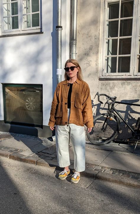 A woman stands in front of a building a bike propped against the wall. She wears a brown chore jacket, black top, white barrel-leg trousers and green and yellow sneakers. Bright Sneakers Outfit, Statement Shoes Outfit, Trousers With Sneakers, Statement Sneakers, Bright Sneakers, Bright Jacket, Trainers Outfit, New Balance Trainers, New Balance Outfit