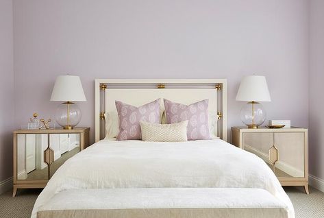 Elegant gold and purple bedroom is furnished with mirrored nightstand topped with glass and brass lamps placed in front of a soft purple painted wall. Soft Purple Bedroom, Purple Bedroom Walls, Purple And Gold Bedroom, Grey And Gold Bedroom, Lilac Bedroom, Lavender Bedroom, Purple Bedrooms, Purple Bedroom, Transitional Bedroom