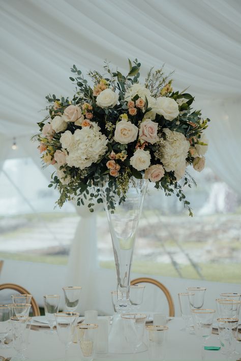 Singular tall, round flower arrangement featuring blush and ivory flowers. Hydrangea roses, miniature roses, lisianthus,  and greenery. the table setting is clear glass with gold accents. Clear Trumpet Vase Tall Centerpiece, Glass Trumpet Vase Centerpiece, Wedding Centerpieces Flowers Tall, Tall Cylinder Vase Centerpiece Wedding, Tall Flower Arrangements Wedding, Tall Wedding Centerpieces Elegant, Trumpet Vase Centerpiece, Modern Wedding Centerpieces, Tall Flower Arrangements