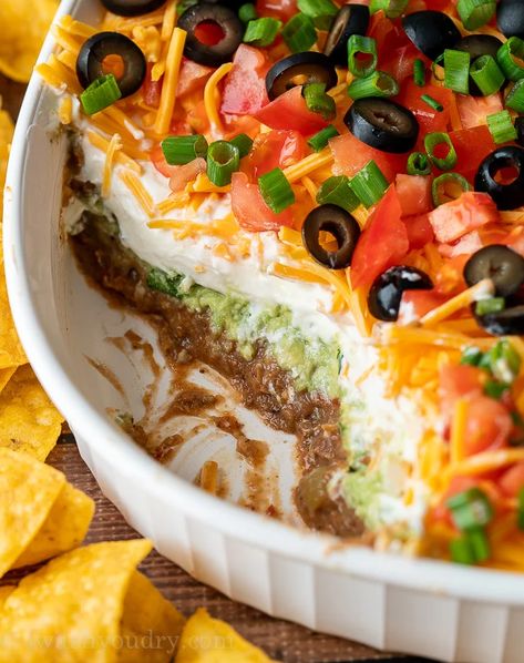 7 Layer Bean Dip with scoop taken out to show layers of beans, guacamole, sour cream and cheese. Spider Web 7 Layer Bean Dip, Seven Layer Mexican Dip, Seven Layer Salad Mexican, Halloween Nacho Dip, Nacho Layer Dip, Easy Birthday Food Ideas, 7 Layer Bean Dip Recipe, Taco Layer Dip, Halloween 7 Layer Dip