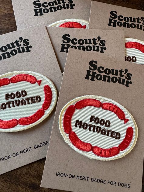 "Does the sight of delicious snacks make your dog weak in the knees? The FOOD MOTIVATED badge is for those dogs who's nose knows no bounds when it comes to tasty treats! Measures approximately 2 1/2\" x 1 3/4\". Oval shaped badge in soft white with dark brown lettering and dark red sausage links around the outer edge. Scout's Honour of the UK makes high quality embroidered patches for your pup's favorite bandana, jacket, vest, harness or sweater.  All of our merit badges are iron-on. It's fuss f Bandana Jacket, Jacket Patches, Scout Badges, Bag Patches, Sausage Links, Merit Badge, Weak In The Knees, Delicious Snacks, Dog Clothing