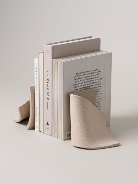 The Serra bookends' form is inspired by the way pages of an old book rest on a dusty shelf, bending and leaning comfortably. Constructed from a singular slab of stoneware, they fold onto themselves in an effortlessly graceful manner. Their simplicity is what makes them striking, with or without books to support. Homemade Book Ends, Ceramic Book Ends Diy, Ceramic Useful Ideas, Soft Slab Ceramics, Pottery Book Ends, Clay Book Holder, Clay Bookends, Simple Ceramic Projects, Books Styling