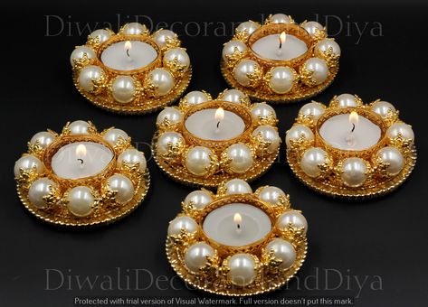 A set of six hand-made tealight candle holders. The regal tealight candle holders are perfect to add glam and charm to any decoration may it be Diwali, Christmas, Eid or a Wedding celebrations. These holders are made up of faux pearls, gota-zari and brass components. PRODUCT DETAILS : The set contains six tealight candle holders. Diameter : 3 inch Height : 1 inch Availability : Ready to ship. Shipped within 24 hours of receiving order. Delivery : Standard delivery FREE through the world. Upgrade Divali Decoration, Designer Rangoli, Diwali Decoration Lights, Plastic Spoon Art, Diwali Candle Holders, Diya Stand, Diwali Gift Box, Aarti Thali, Tea Light Holder Wedding