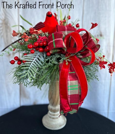 Bring the beauty of nature into your home this holiday season with this handcrafted Christmas floral arrangement featuring a charming red cardinal perched among lush evergreen branches, bright red berries, and a festive plaid and velvet ribbon. Nestled in a rustic wooden base, this arrangement is perfect for a mantelpiece, table centerpiece, or a holiday gift for loved ones. Its timeless design captures the spirit of winter and adds a cheerful touch to any décor. Order now to make your holiday season more special! Candle Stick Christmas Centerpiece, Christmas Pedestal Decor, Centerpiece Christmas Table Diy, Cardinal Decorations Holidays, Christmas Silk Arrangements, Christmas Candlestick Centerpiece, Christmas Candlestick Arrangements, Christmas Silk Floral Arrangements, Red And Green Christmas Decor Ideas