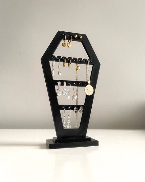 Our black Coffin Earring and Jewelry stand will add a touch of spooky elegance to your jewelry collection. This unique stand features four sections with several holes to accommodate various earring styles, including studs, small hoops, and dangle earrings. The stand also has some grooves, allowing you to hang delicate necklaces. #HandmadeJewelry #StatementJewelry #Accessories #Fashion #Style #Gemstone #JewelryDesign #Jewelry #JewelryAddict #JewelryLovers Coffin Jewelry Holder, Goth Diy, Coffin Decor, Gothic Homeware, Earring Holder Stand, Gothic Decor Bedroom, Glowforge Ideas, Jewellery Stand, Gothic Jewellery