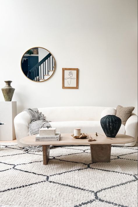 Neutral white living room with curved couch and oval wooden coffee table Oval Living Room Table, Oval Live Edge Coffee Table, How To Style Oval Coffee Table, Long Oval Coffee Table, Wooden Oval Coffee Table, Diy Coffee Table Oval, Modern Oval Coffee Table, Oblong Coffee Table, Diy Oval Table